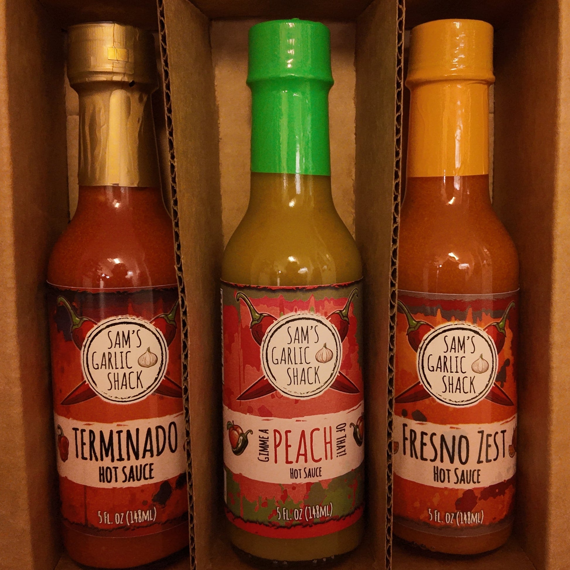 Three hot sauce bottles in a cardboard box on a dark background